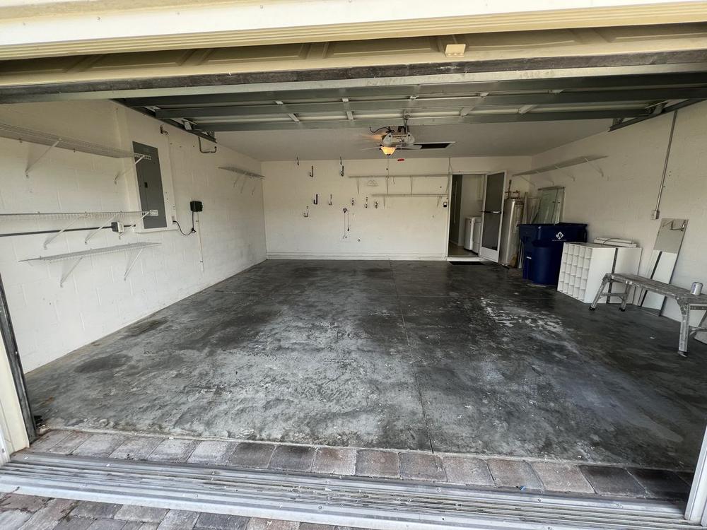 The same garage swept back to bare concrete, wide open from the door to the back wall, with a refrigerator and two bins tucked into the far corner.