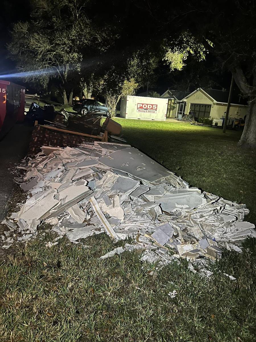 A driveway stacked with stripped drywall sheets and remodel debris outside an active job site.