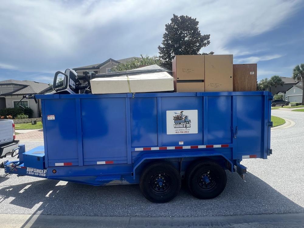 The blue Warriors of Junk trailer parked at the kerb on a residential street, loaded level with flattened cardboard and boxes.