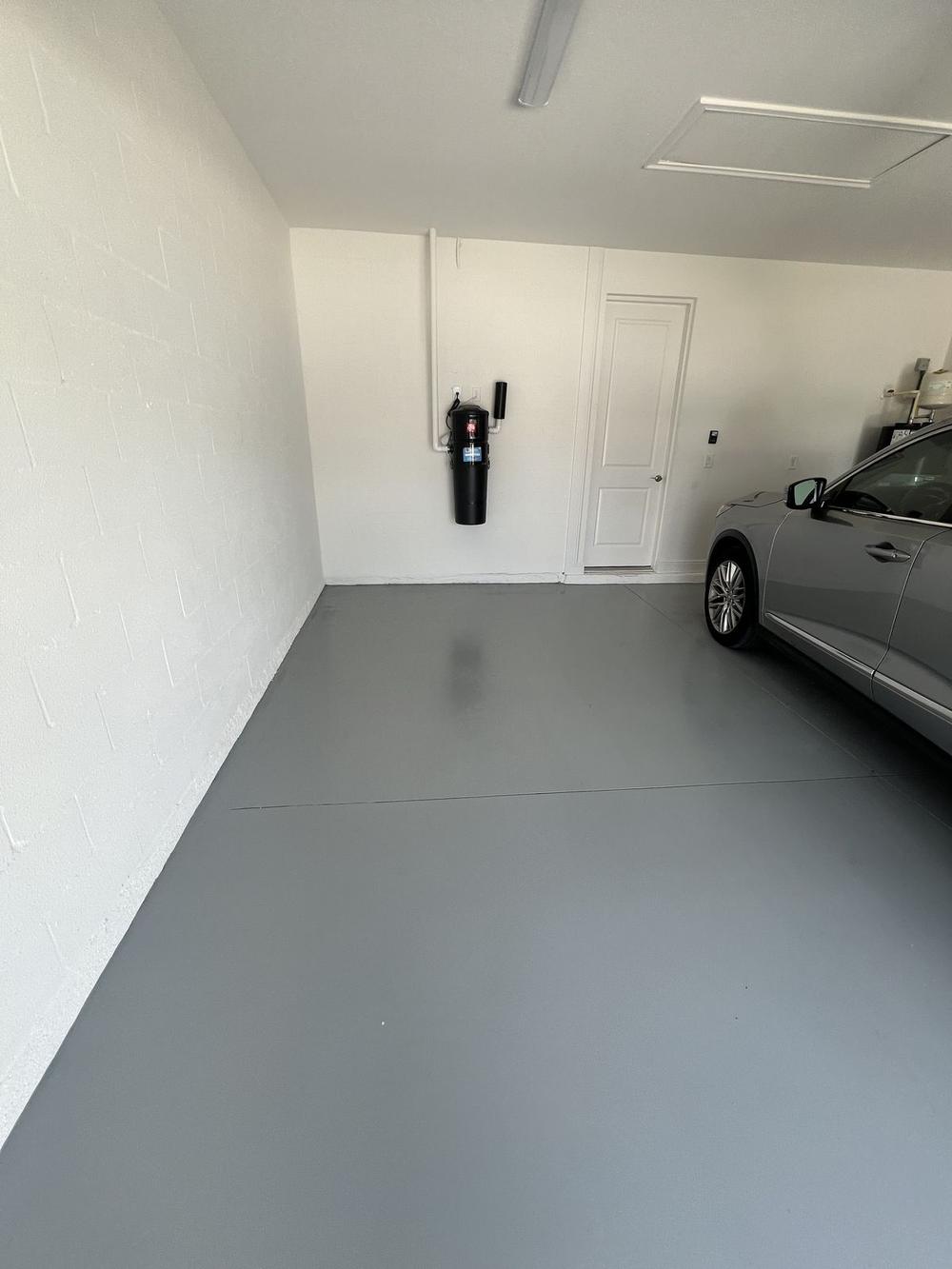 A finished garage with a clean swept floor and a car parked back inside it, the wall panel and door clear of everything that used to be stacked against them.