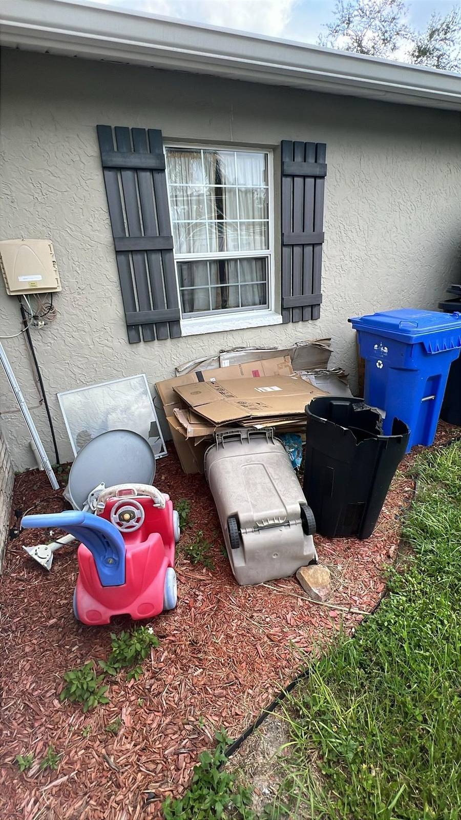 A mixed pile set out beside a house for collection: a patio chair, a folding table, blue bins and bagged household waste.